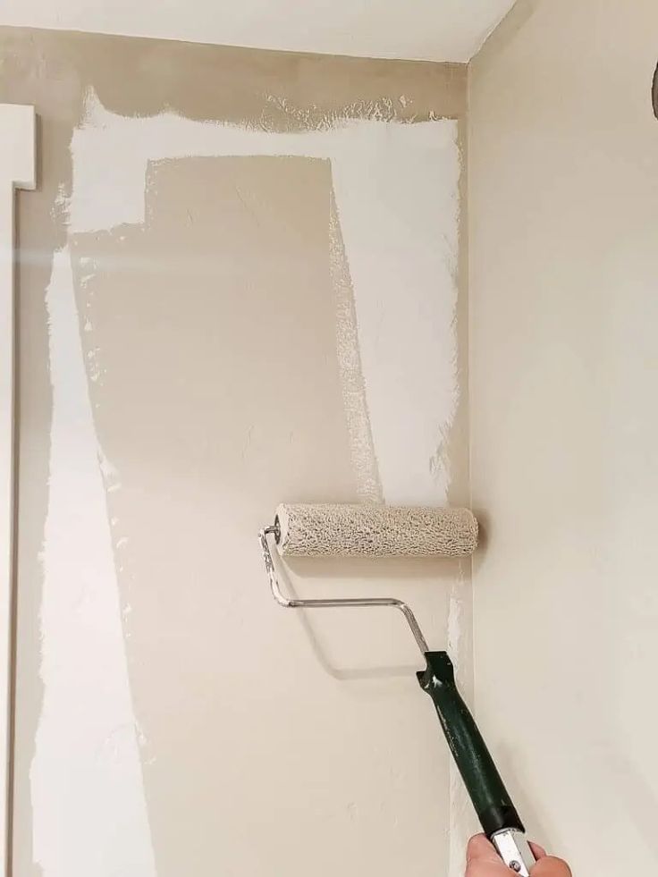 a person is painting the walls with white paint and a green brush in their hand