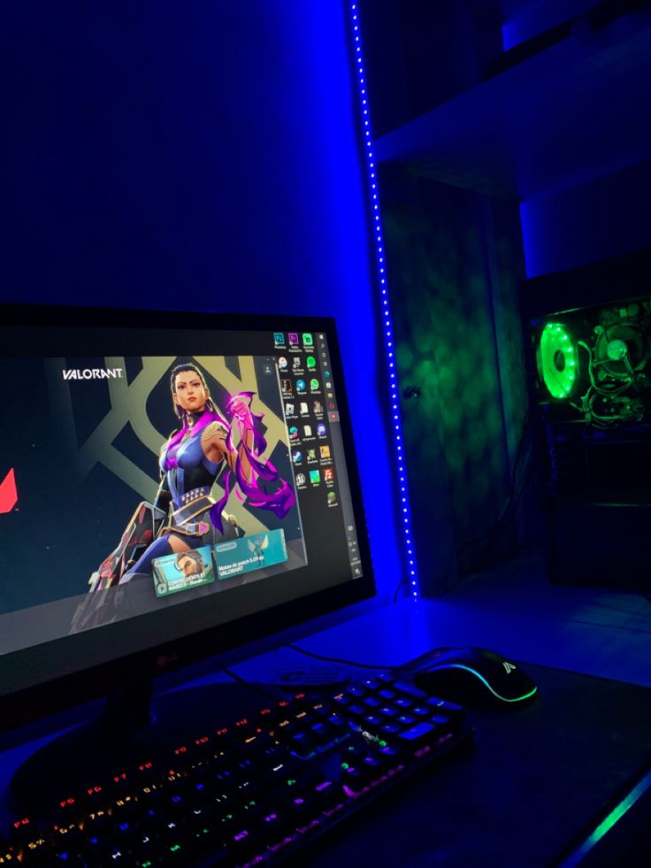 a computer monitor and keyboard lit up in the dark with neon lights behind it on a desk