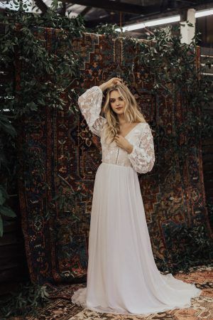 a woman standing in front of an area rug wearing a white dress with long sleeves