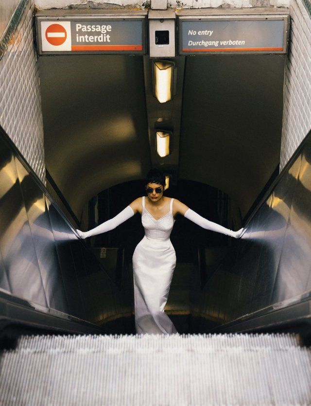 a woman in white dress walking down an escalator with her arms out and hands outstretched