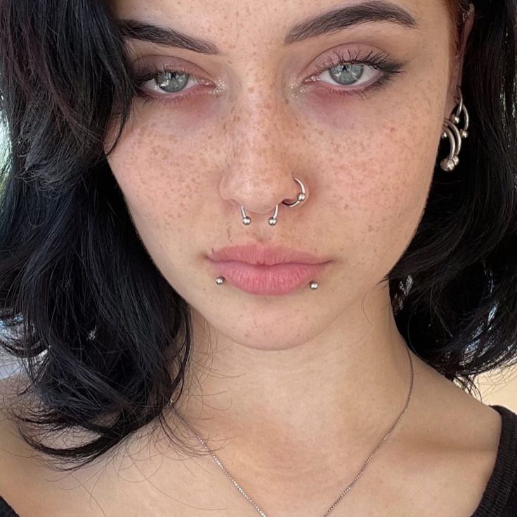 a woman with freckles and piercings on her nose looking at the camera