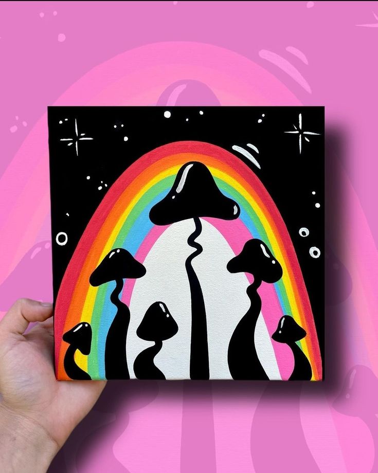 a person holding up a painting with mushrooms and rainbows in the background on a pink wall