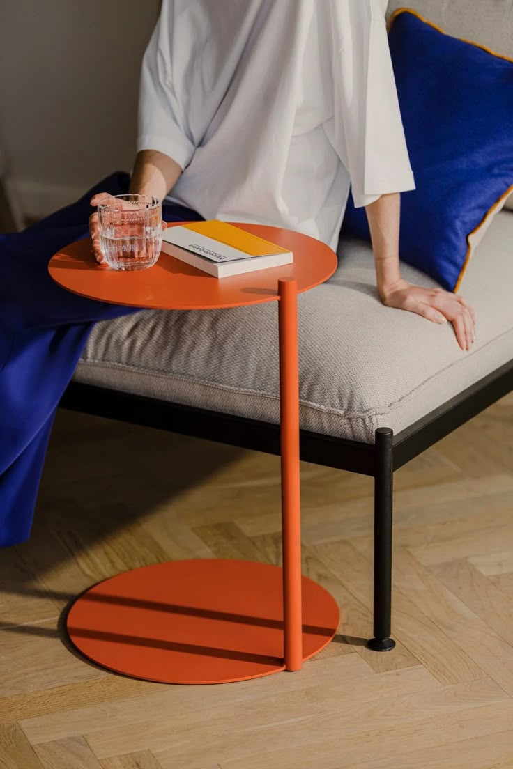 a woman sitting on a couch next to a table with a book and drink in it