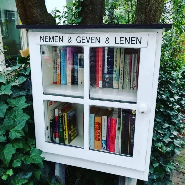 a book shelf with books on it in front of a tree and bushes, next to a sign that reads nemen & given & lenn