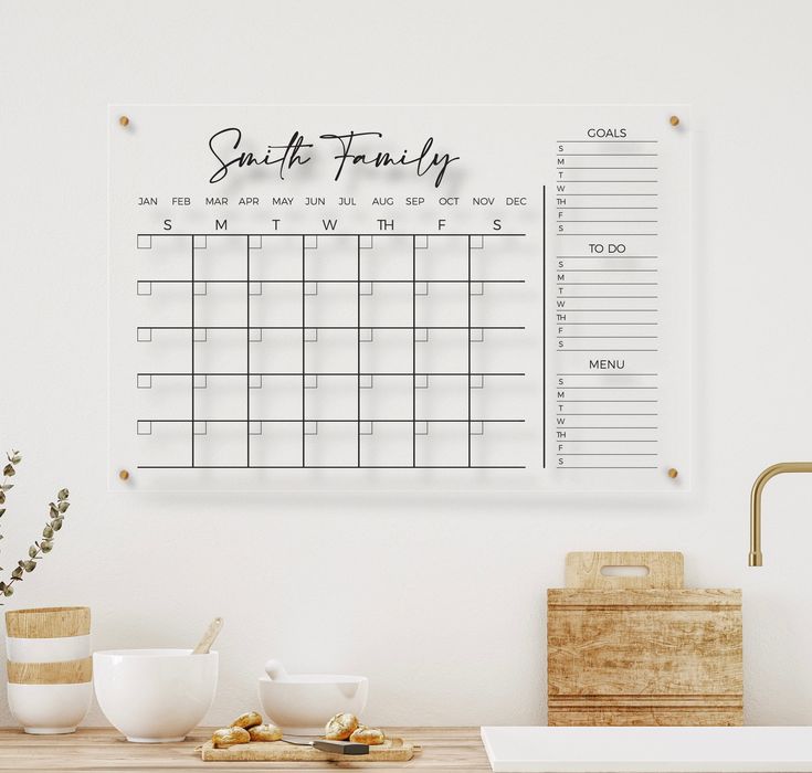 a calendar hangs on the wall above a wooden table with coffee cups and other items