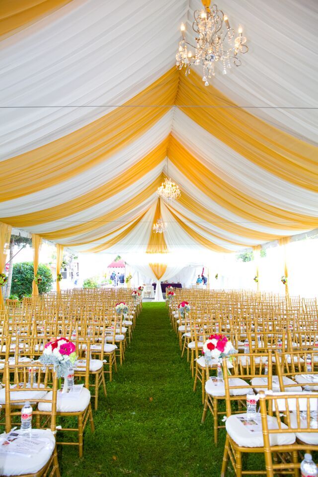 rows of chairs set up in front of a white and yellow tent with chandelier