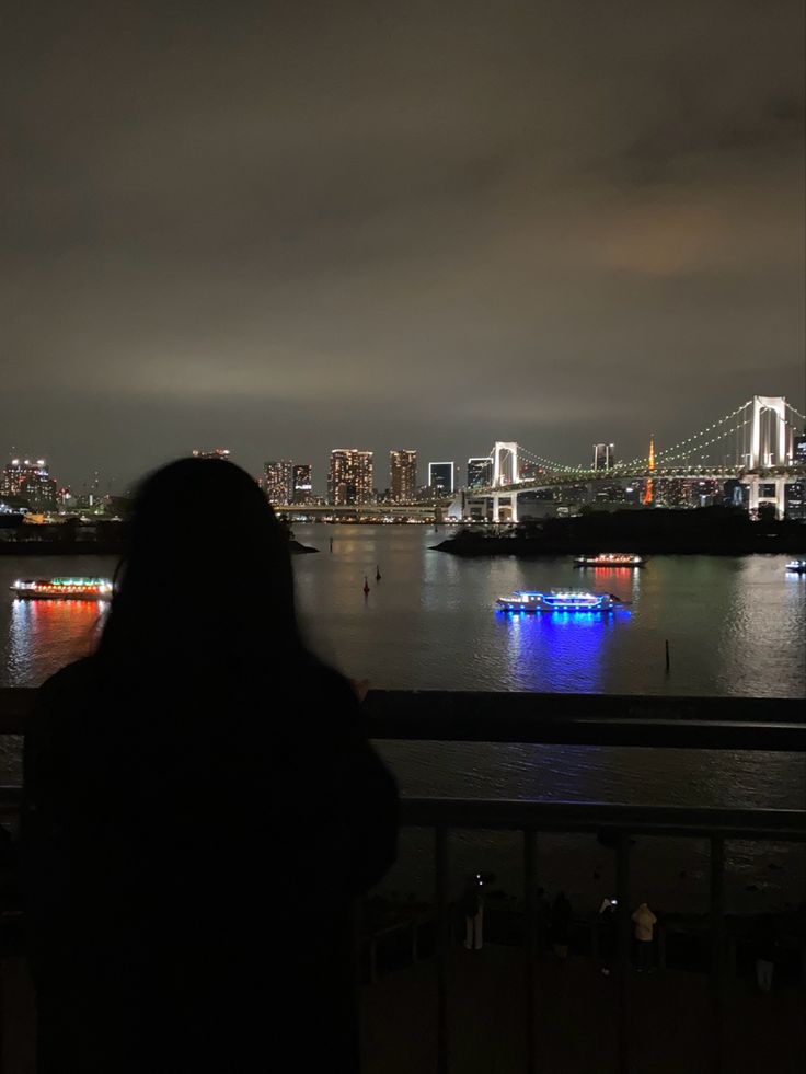 a person is looking out over the water at night with lights on them and boats in the water