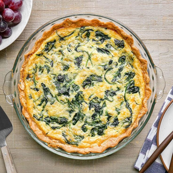 a quiche with spinach and cheese in a glass pie dish on a wooden table