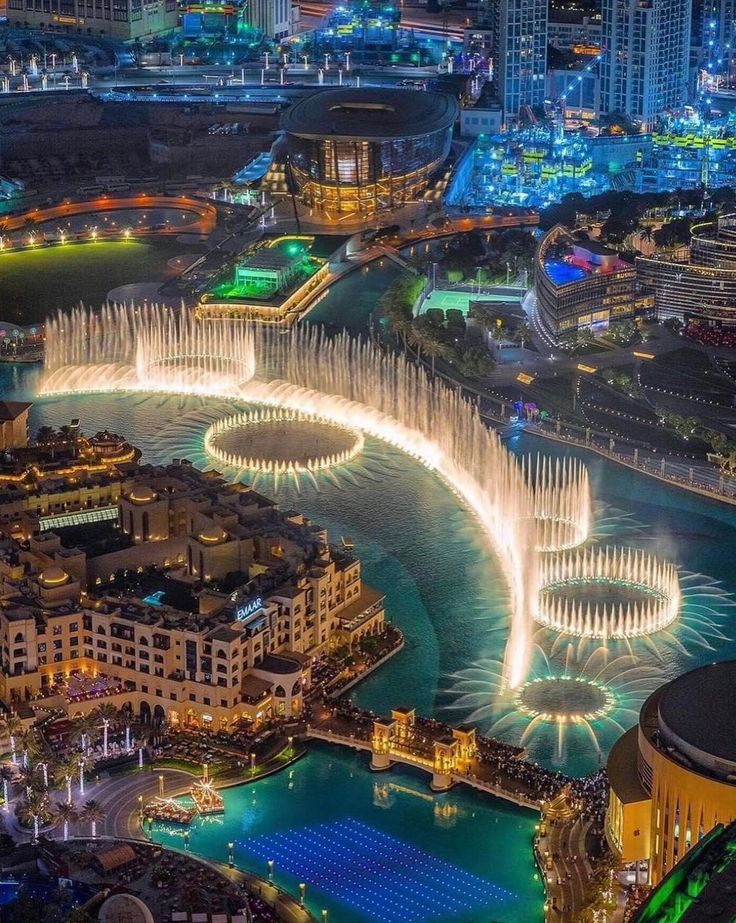 an aerial view of a city with fountains in the water and buildings around it at night