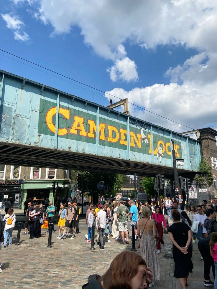 a crowd of people walking under an overpass with the words camden lock on it