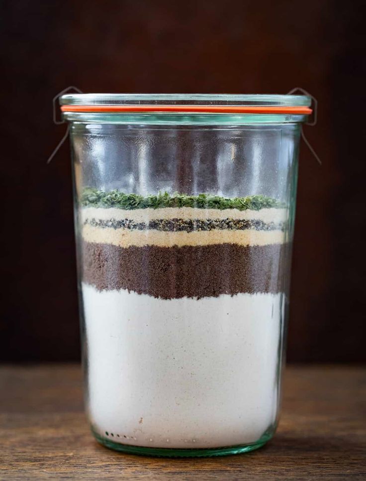 a glass jar filled with brown, white and green ingredients on top of a wooden table