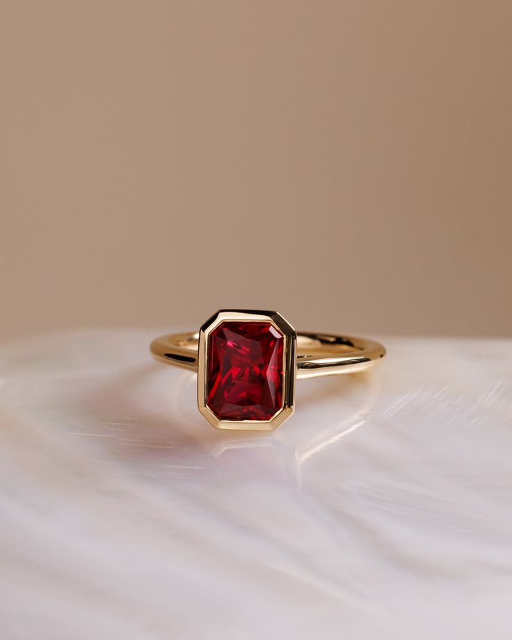 a gold ring with a red stone in the center on a white surface, close up