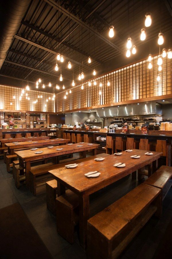 a restaurant with wooden tables and benches in front of the counter area, along with lights hanging from the ceiling