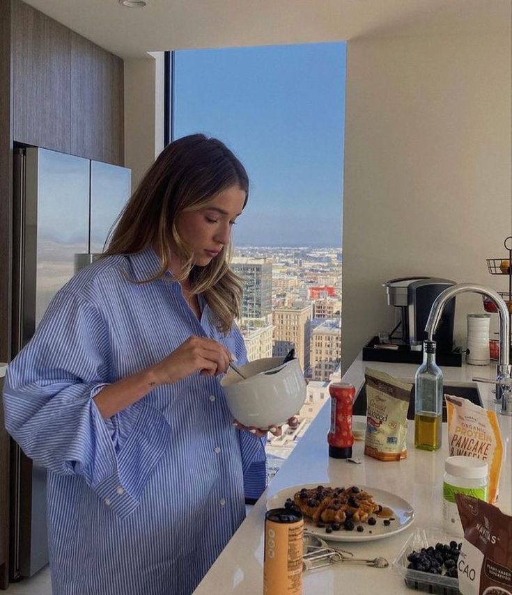 a woman standing in front of a kitchen counter holding a bowl with food on it