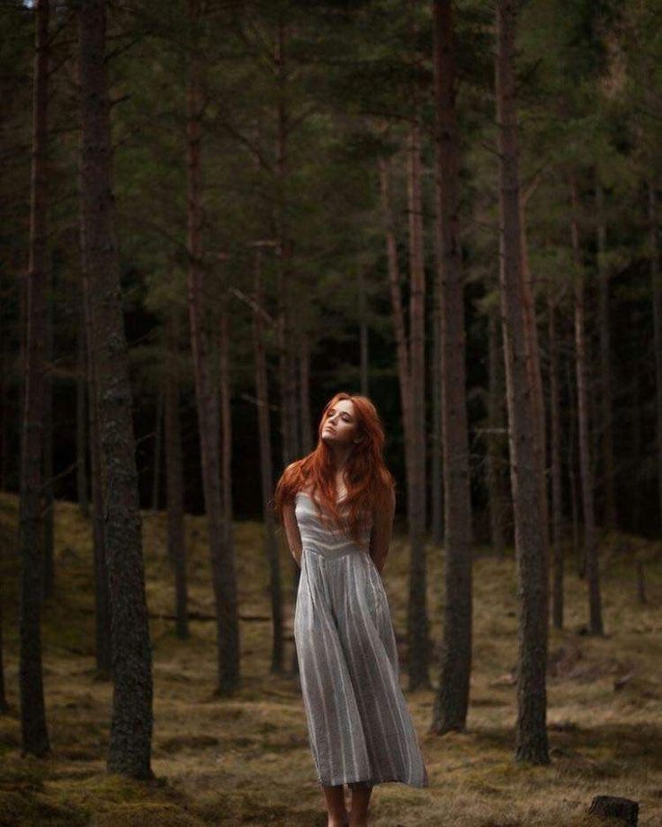 a woman with red hair standing in the woods