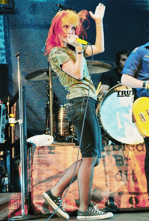 a woman with pink hair singing into a microphone while standing next to a man holding a guitar