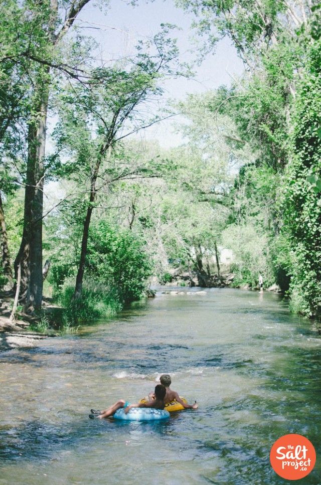 a man riding on top of a blue raft down a river surrounded by trees and bushes