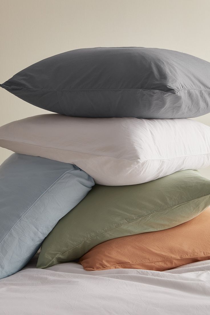 four pillows stacked on top of each other in different colors and sizes, all piled up together