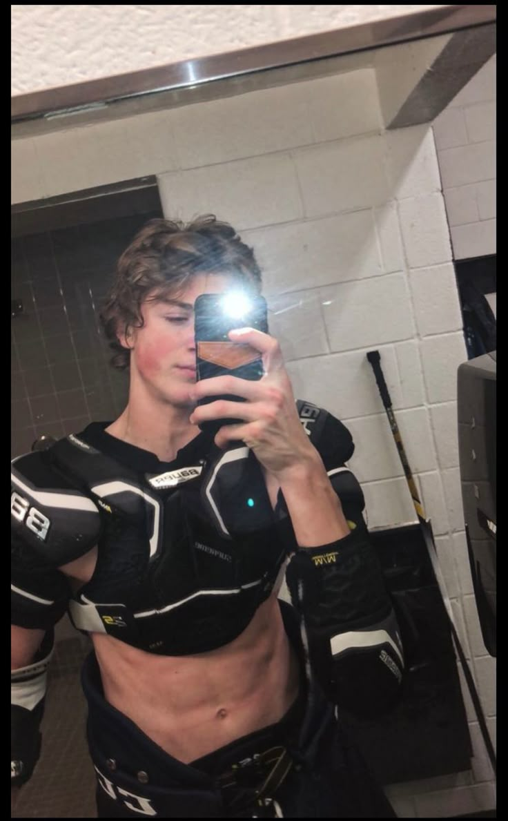 a man taking a selfie in the mirror with his cell phone while wearing a hockey uniform