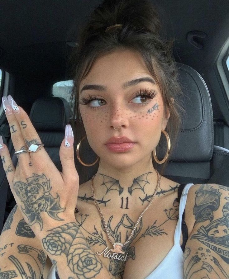 a woman with tattoos on her arms and chest holding up two fingers in the back seat of a car