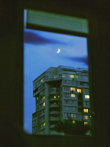 the moon is seen through an open window in a building at night with lights on