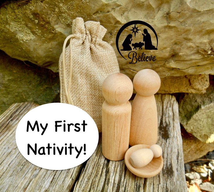 two wooden pegs sitting next to a bag with the words my first nativity