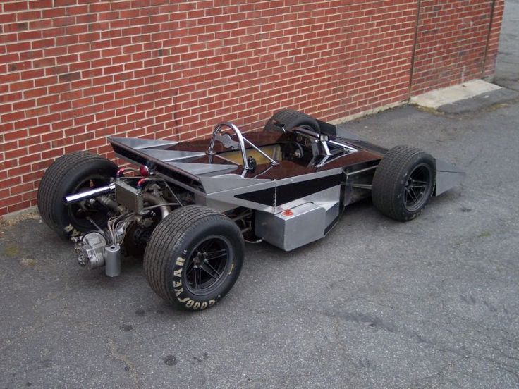 an unusual looking car is parked in front of a brick wall on the side of a street