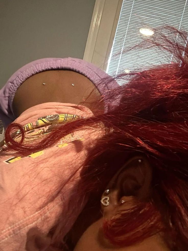 a woman with red hair laying on her stomach and wearing ear piercings in front of a window