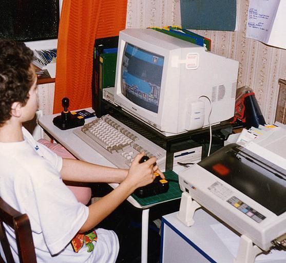 a young boy sitting at a desk with an old computer and printer in front of him