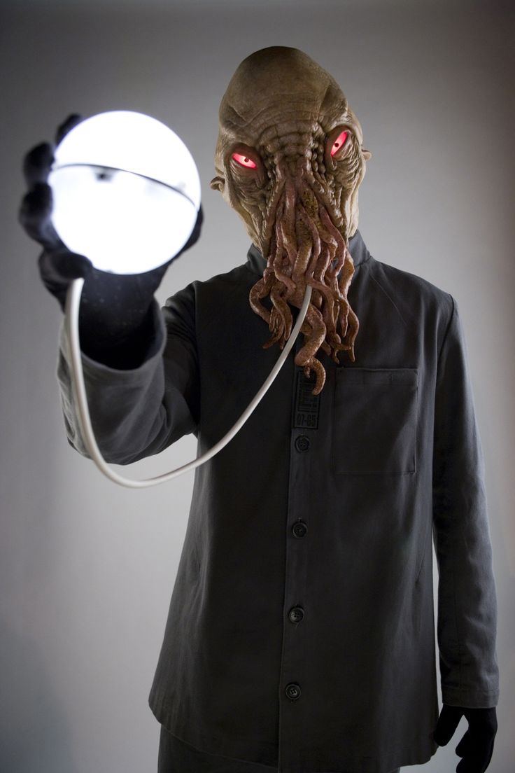 a man in a black shirt holding a white light up object with red eyes and an octopus like head