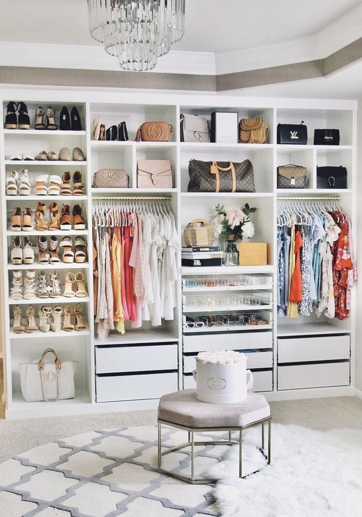 a white closet filled with lots of shoes and handbags on top of shelves next to a chandelier