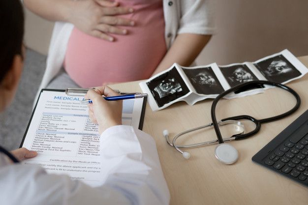 a pregnant woman sitting at a desk in front of a doctor's clipboard