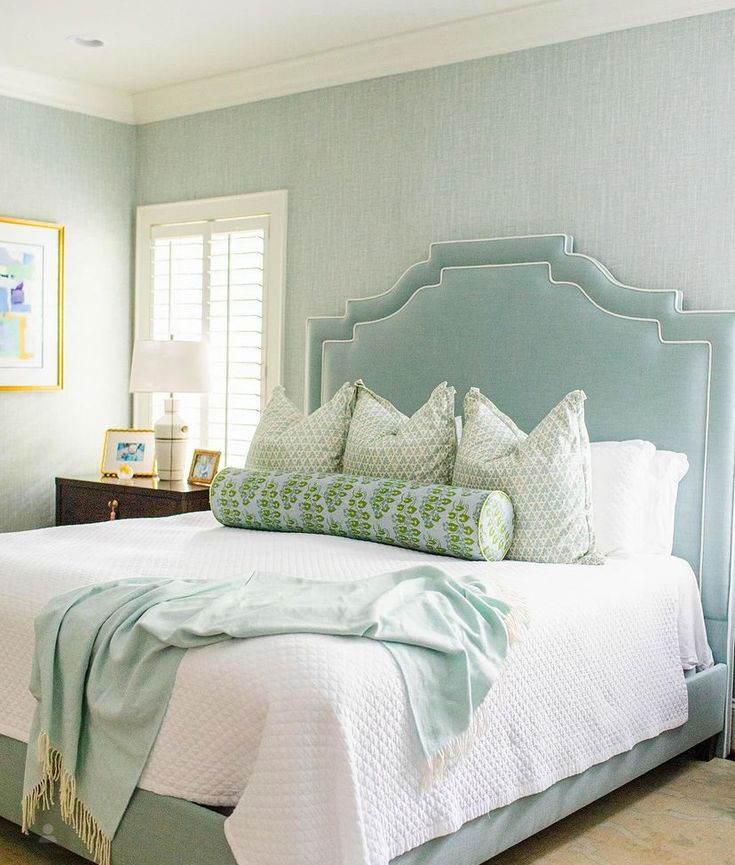 a bedroom with blue walls, white bedding and green accents on the headboard