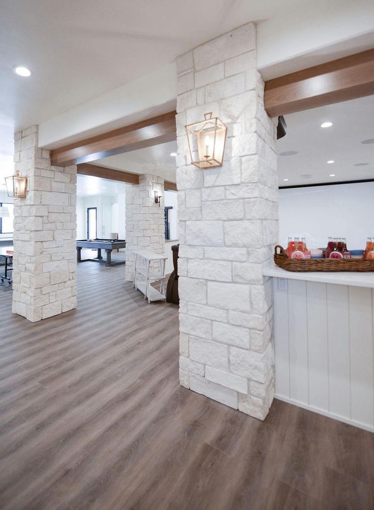 an empty room with wood flooring and white brick pillars in the center, along with tables and chairs