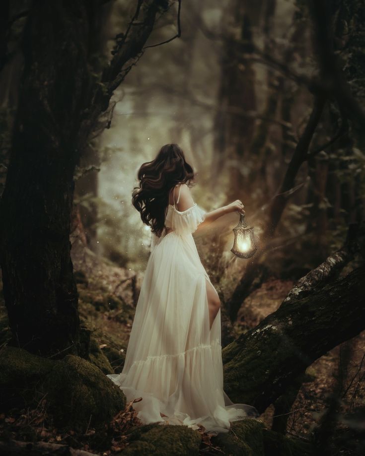 a woman in a white dress holding a lantern standing on a mossy forest floor