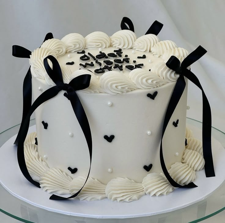 a white cake with black bows and hearts on top is sitting on a glass plate