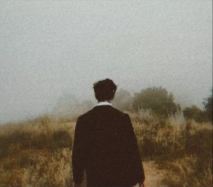 a man walking down a dirt road in the middle of a dry grass covered field