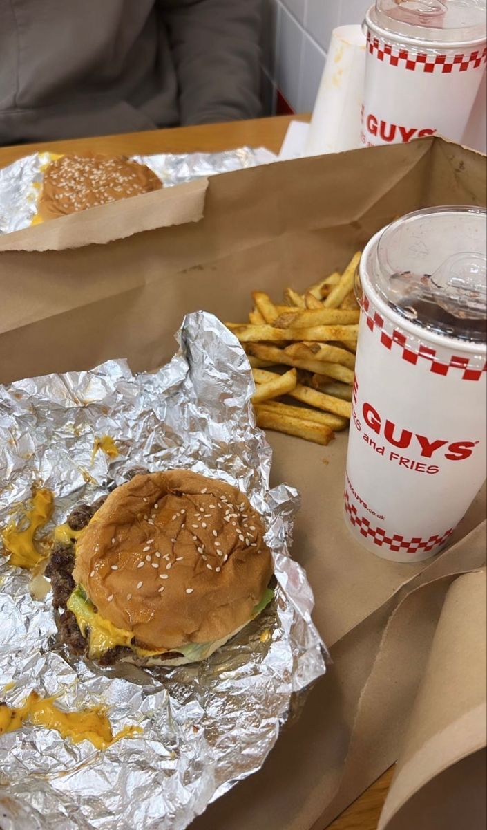 a hamburger and french fries are sitting on tin foil next to a cup of coffee