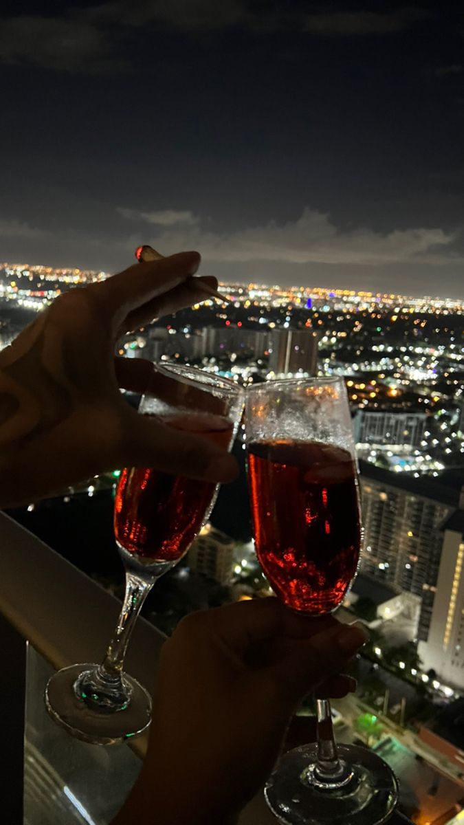 two people toasting with red wine in front of a cityscape at night