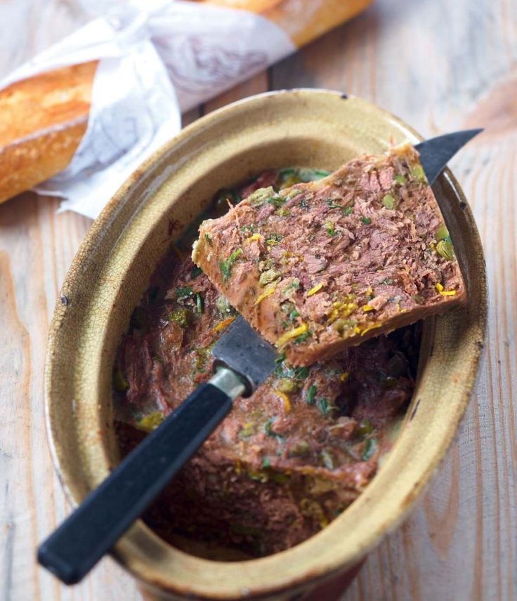 a wooden bowl filled with food on top of a table next to bread and baguette