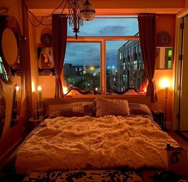 a large bed sitting in front of a window next to a night stand with candles on it