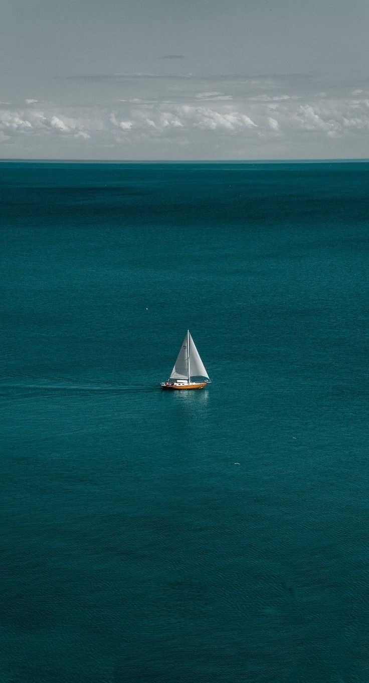 a sailboat floating in the middle of an ocean with blue water and white clouds