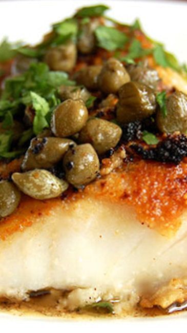 a white plate topped with fish covered in olives