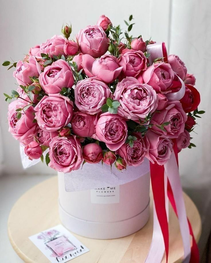 a large bouquet of pink roses in a white hat box on a table with a red ribbon