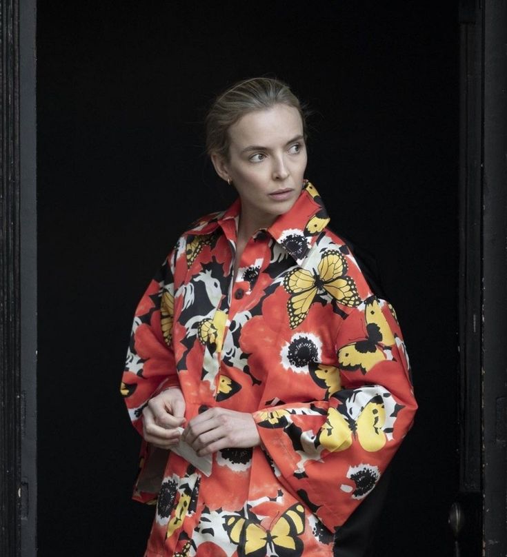 a woman standing in front of a black background wearing an orange and yellow flowered shirt