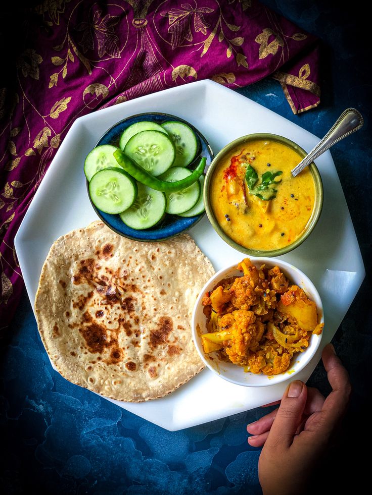 a person holding a plate with food on it and cucumbers, bread, and sauce