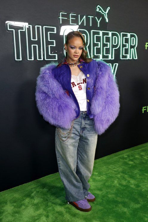 a woman in purple fur coat and jeans at the green carpet awards ceremony, with her hands on her hips