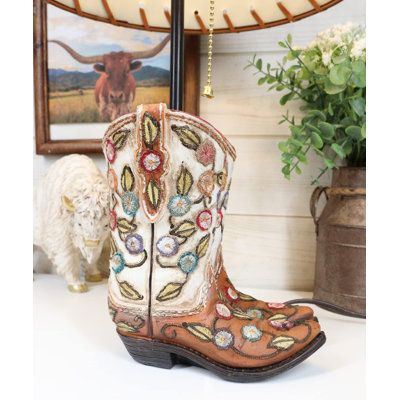 This western boots table lamp comes with the shade as pictured. Made of polyresin, hand-painted and polished, the quality finish is superb! The shade is made of laced paper textured in a leather-like finish. The top and bottom fringes of the shade has lace stripes. Foundry Select | Foundry Select Figurine 19.0 H x 12.0 W x 12.0 D in brown / orange / pinkResin / Paper in Blue;orange | 19" H X 12" W X 12" D | Wayfair Tan Cowgirl Boots, Hippy Aesthetic, Desktop Table, Modest Clothes, Western Rustic, Embroidery Hand, Brown Shades, Tooled Leather, Christmas Wishlist