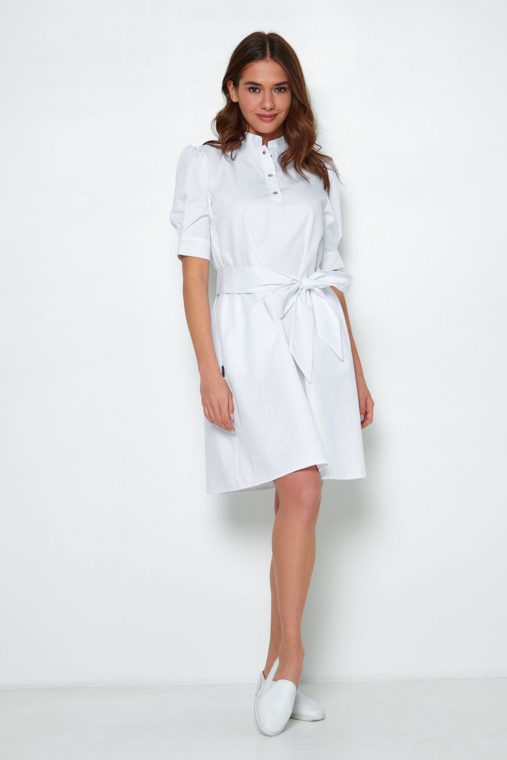 This fashionable uniform scrub dress will make any female doctor or a beautician look stylish and classy when at work.  The  lab coat has a babydoll design, a full skirt, and short full volume sleeves decorated with crystal embroidery. Convenient length and relaxed fit will fit any type of figure. The scrub dress has a detachable belt and cutouts on the sleeves. The fabric is 70% cotton, 30% polyester, made in the Netherlands. Your customers will get aesthetic pleasure when communicating with yo Esthetician Uniform, Scrub Dress, Scrubs Women, Nurse Dress Uniform, Scrubs Nursing Uniforms, White Scrubs, Scrubs Dress, Medical Lab, Doctor Outfit