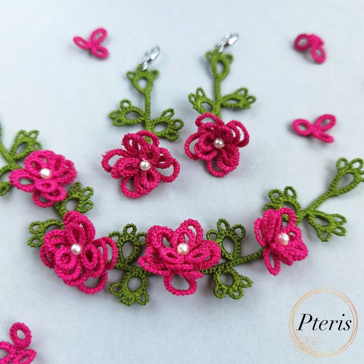 pink and green crocheted flowers with pearls in the center on a white surface